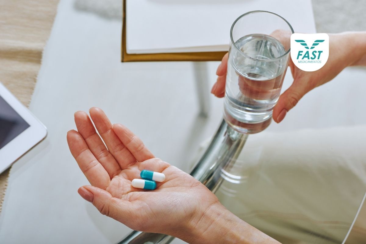 Pessoa com medicamento e copo de água na mão